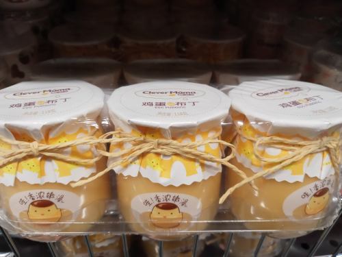 Three jars of pudding with a cute design, tied with twine, displayed on a shelf.