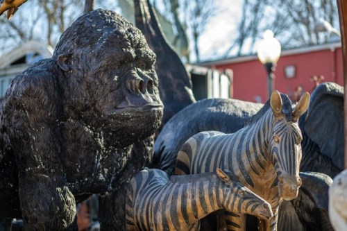 A close-up of a large black gorilla statue alongside several zebra statues in a park setting.