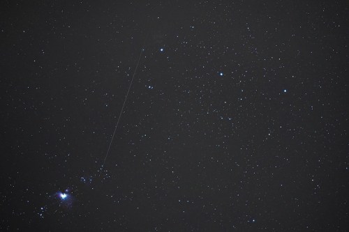 A starry night sky filled with numerous stars and a faint streak, possibly a meteor, against a dark backdrop.