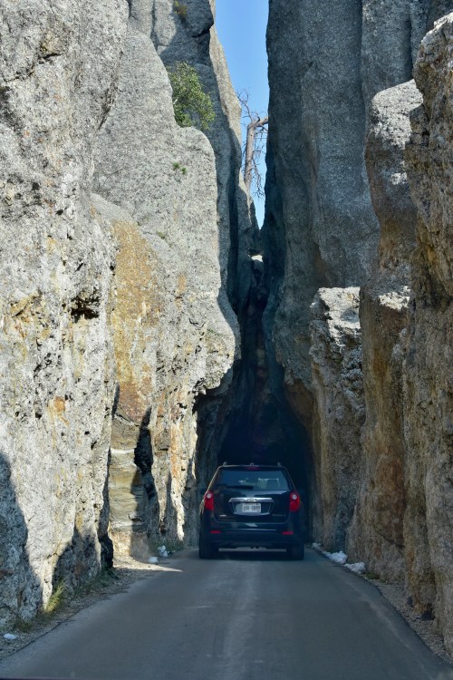 A car drives through a narrow canyon surrounded by towering rock formations.