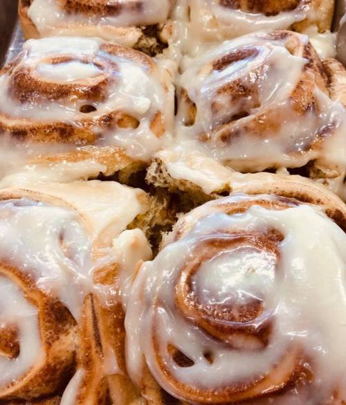 Freshly baked cinnamon rolls topped with creamy icing, arranged closely together.