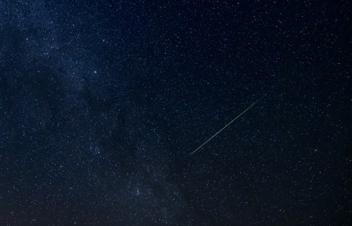 A starry night sky filled with countless stars and a bright meteor streaking across the scene.