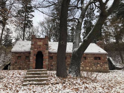 A stone building surrounded by snow-covered ground and trees, with steps leading up to the entrance.