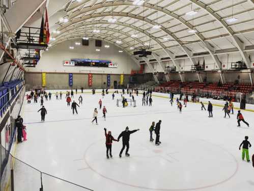 A busy ice skating rink with many skaters enjoying the ice under a large, arched roof.