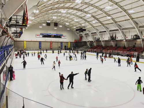 A busy ice skating rink with many skaters enjoying the ice under a large, arched roof.