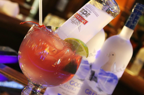 A colorful cocktail garnished with a cherry and lime, featuring a bottle of vodka resting inside the glass.