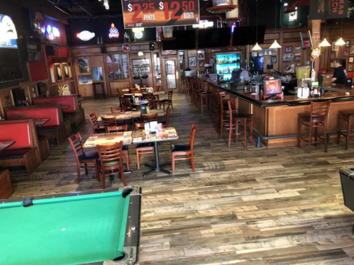 A spacious bar interior with wooden floors, booths, tables, and a pool table, featuring a well-stocked bar area.