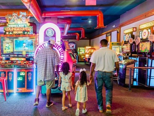 Two adults and two children walk towards colorful arcade games in a vibrant gaming center.