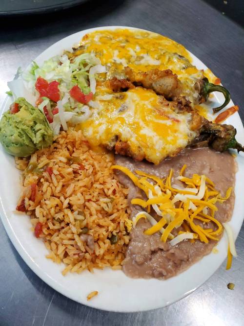 A plate of enchiladas topped with cheese, served with rice, refried beans, lettuce, tomatoes, and guacamole.