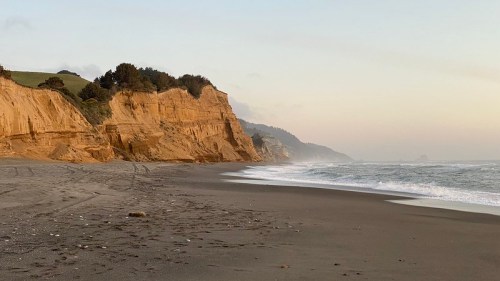 A serene beach scene with sandy cliffs, gentle waves, and a soft sunset glow in the background.