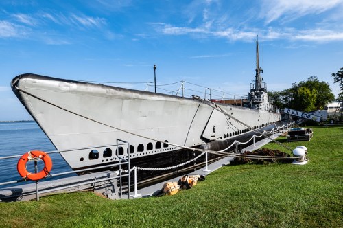 A historic submarine docked by the water, with a clear blue sky and green grass in the foreground.