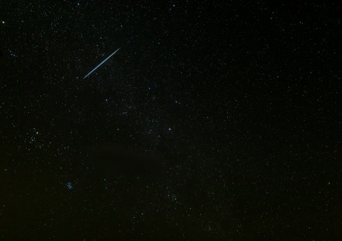 A starry night sky filled with countless stars and a bright meteor streaking across the darkness.
