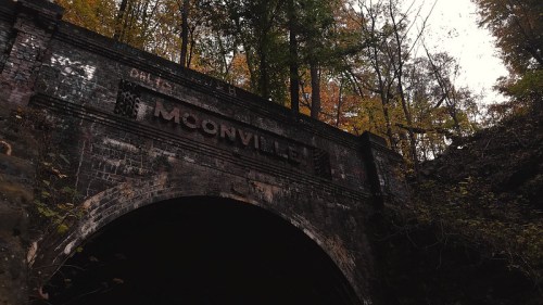 A dark tunnel entrance with "Moonville" engraved above, surrounded by trees with autumn foliage.