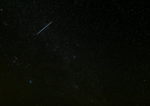 A starry night sky filled with countless stars and a bright meteor streaking across the darkness.