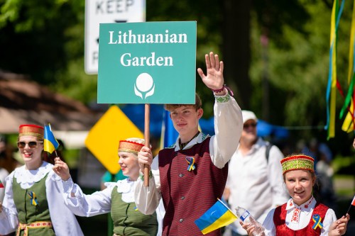 A group of people in traditional attire holding a sign that reads "Lithuanian Garden" during a parade.