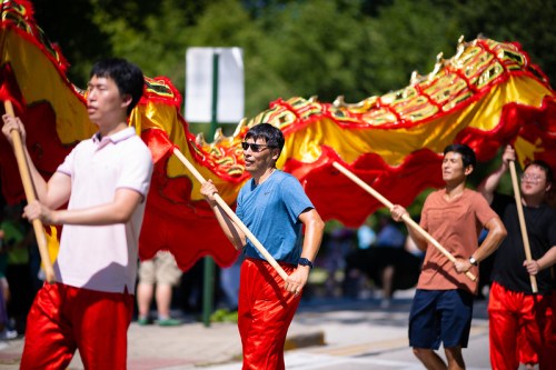 Participants in colorful outfits carry a large dragon costume during a festive parade.