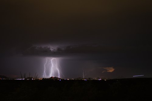 A dramatic night sky illuminated by lightning strikes over a distant city, with dark clouds and a hint of urban lights.