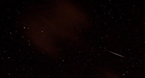 A night sky filled with stars, featuring a bright meteor streaking across the darkness.