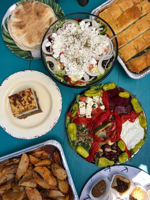 A colorful spread of Mediterranean dishes, including salad, pastries, roasted potatoes, and desserts on a blue table.