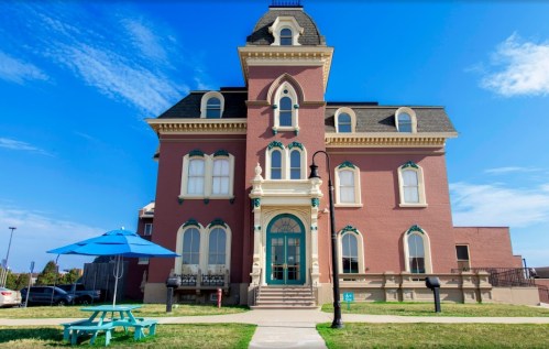Historic brick building with ornate architecture, featuring a blue umbrella table in front and a clear blue sky.