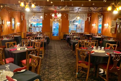 Cozy restaurant interior with dark tables, red accents, and warm lighting, set for dining with elegant decor.
