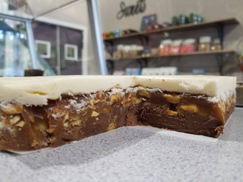 Close-up of layered fudge with a creamy white top, chocolate base, and nuts, displayed on a countertop.