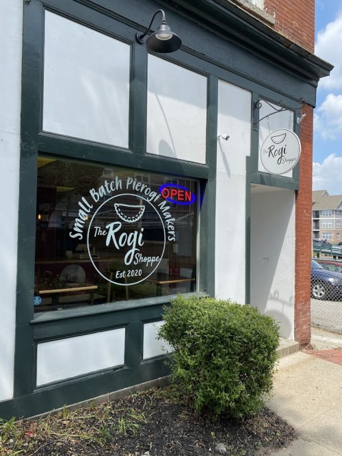 Exterior of The Rogi Sheppe, a small batch pierogi shop, featuring a sign and an open window. Established 2020.