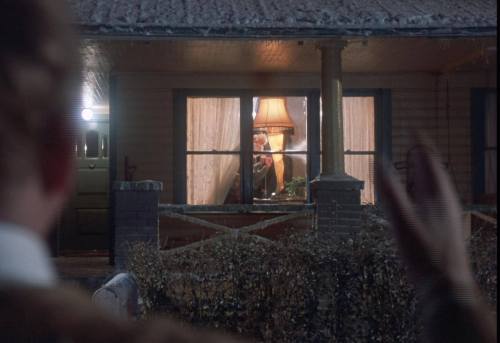 A person waves from outside a house, with a warm lamp glowing in the window, creating a cozy atmosphere.
