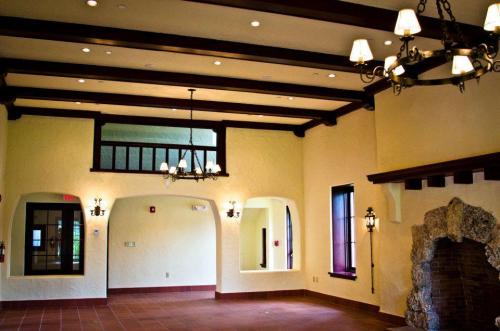 Interior of a spacious room with wooden beams, chandeliers, and arched doorways, featuring a stone fireplace.
