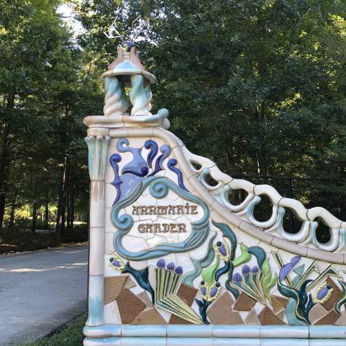 A decorative entrance sign for "Ariel's Garden" surrounded by lush greenery and trees.