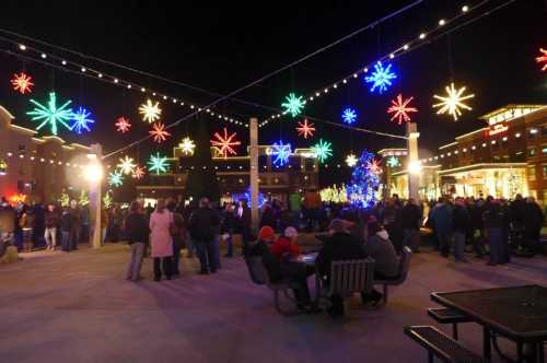 A festive night scene with colorful snowflake lights and a crowd enjoying a holiday event in a plaza.