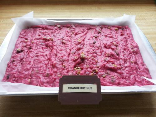 A rectangular tray of cranberry nut fudge, pink in color, with a label reading "Cranberry Nut" in front.