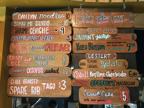Menu board featuring dishes like catfish curry, shrimp ceviche, and desserts like key lime cheesecake and gelato.