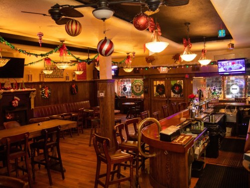 Cozy bar interior decorated for the holidays, featuring festive lights, ornaments, and a wooden bar with seating.