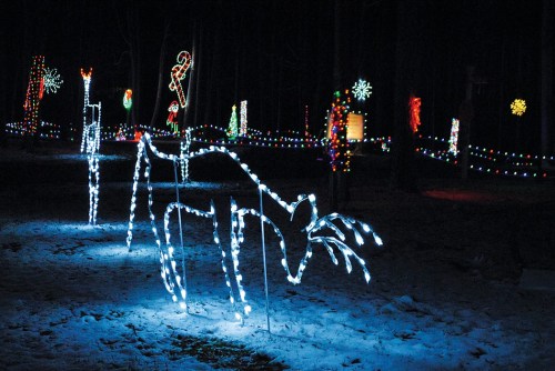 A glowing reindeer made of lights stands in a snowy landscape, surrounded by colorful holiday decorations.