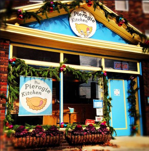 A festive storefront of The Pierogie Kitchen, decorated with garlands and holiday ornaments, with an "Open" sign.