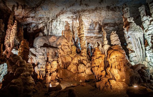 Stalactites and stalagmites in a beautifully lit cave, showcasing intricate rock formations and textures.