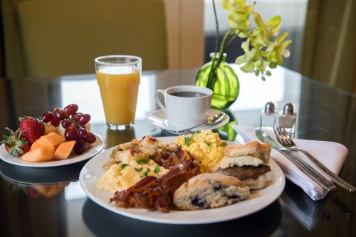 A breakfast spread with scrambled eggs, bacon, biscuits, fruit, coffee, and orange juice on a table.