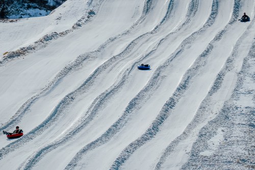 People sledding down snowy slopes on colorful tubes, with distinct tracks in the snow.