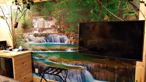 A wall mural of a serene waterfall scene with lush greenery, alongside a mounted TV and wooden furniture.
