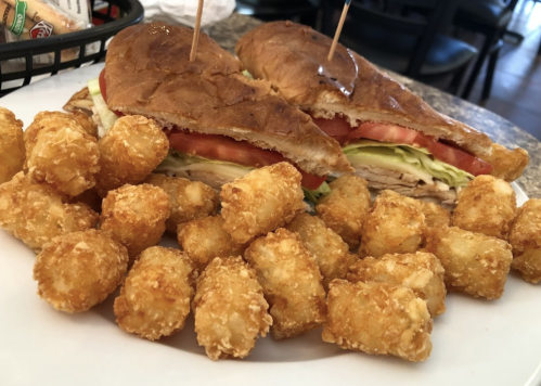 A plate featuring a sandwich with turkey, lettuce, and tomato, accompanied by a side of crispy tater tots.