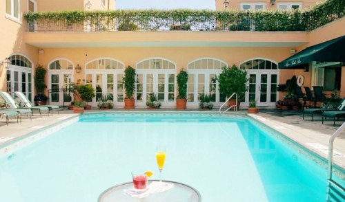 A serene pool area with two cocktails on a table, surrounded by lush greenery and elegant architecture.