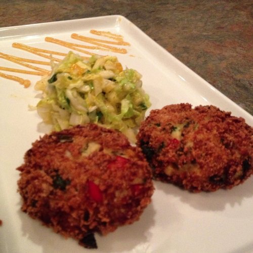 Two golden-brown fritters on a white plate, accompanied by a small serving of shredded cabbage and a drizzle of sauce.
