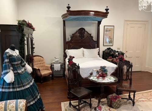 A vintage bedroom featuring a four-poster bed, antique furniture, and a decorative dress on display.