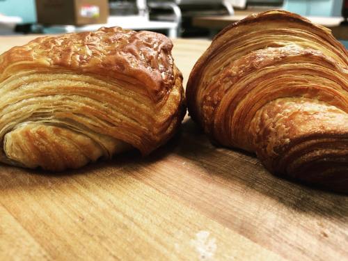 Two freshly baked croissants with golden, flaky layers resting on a wooden surface.