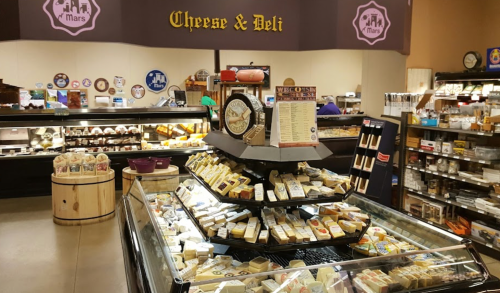 A cheese and deli shop featuring a display of various cheeses and a vintage scale, with a welcoming atmosphere.