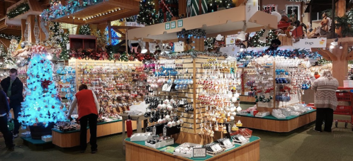 A festive store filled with colorful ornaments and decorations, with shoppers browsing among Christmas displays.