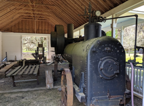 A vintage steam engine displayed in a rustic shed, showcasing its black metal body and wooden surroundings.