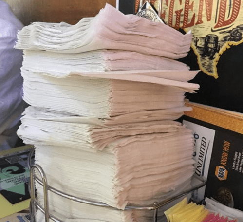 A tall stack of white napkins in a metal holder on a table, with colorful sticky notes in the background.