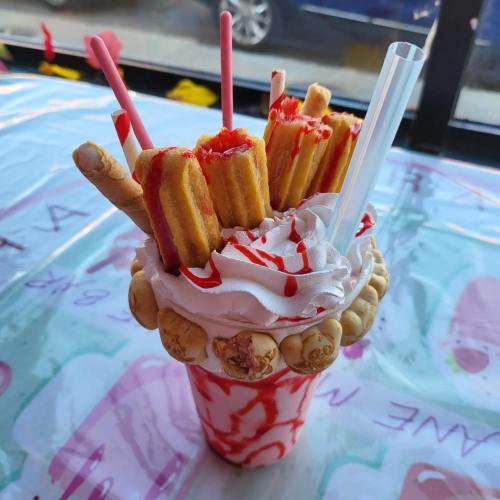 A colorful milkshake topped with whipped cream, candy, and mini waffles, served in a festive cup with straws.
